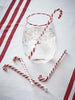 Clear glass with ice cubes and candy canes on a red and white striped surface